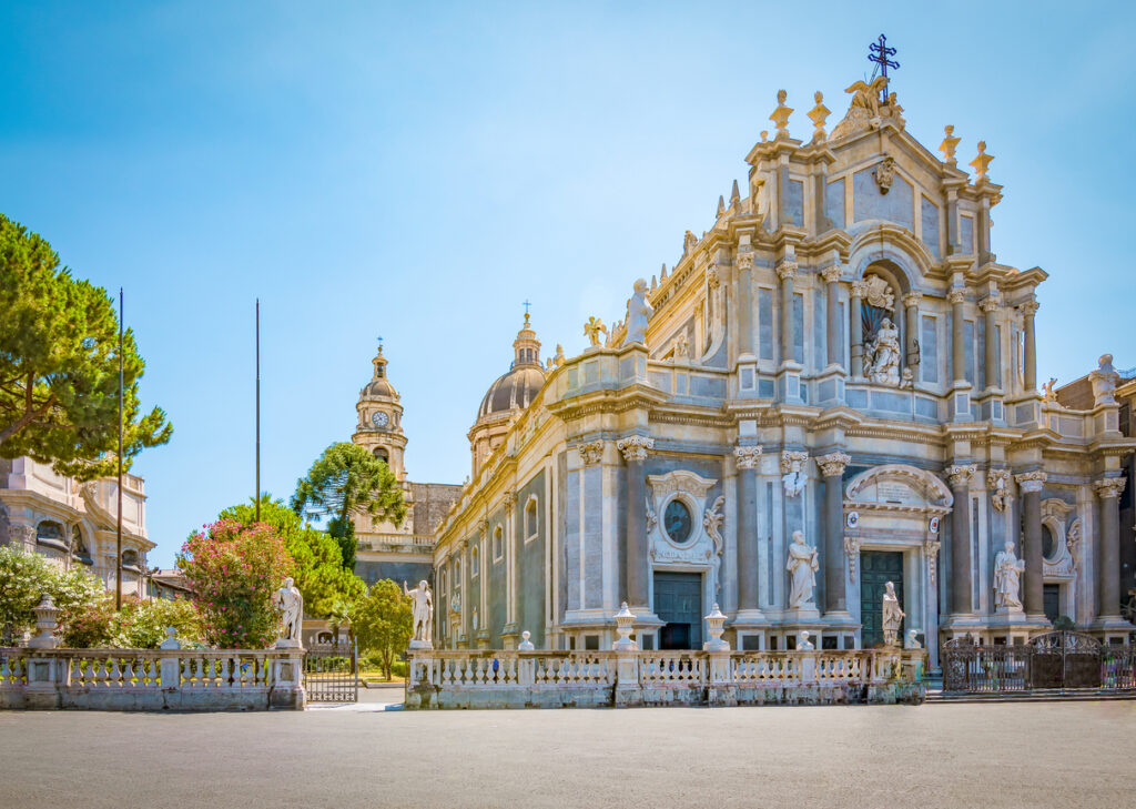 Fassade der Kathedrale von Catania mit Figuren und Kuppeln unter blauem Himmel.
