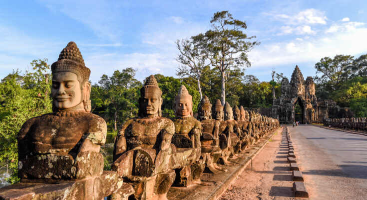 Reihen steinerner Devas führen zur Toranlage im Wald.