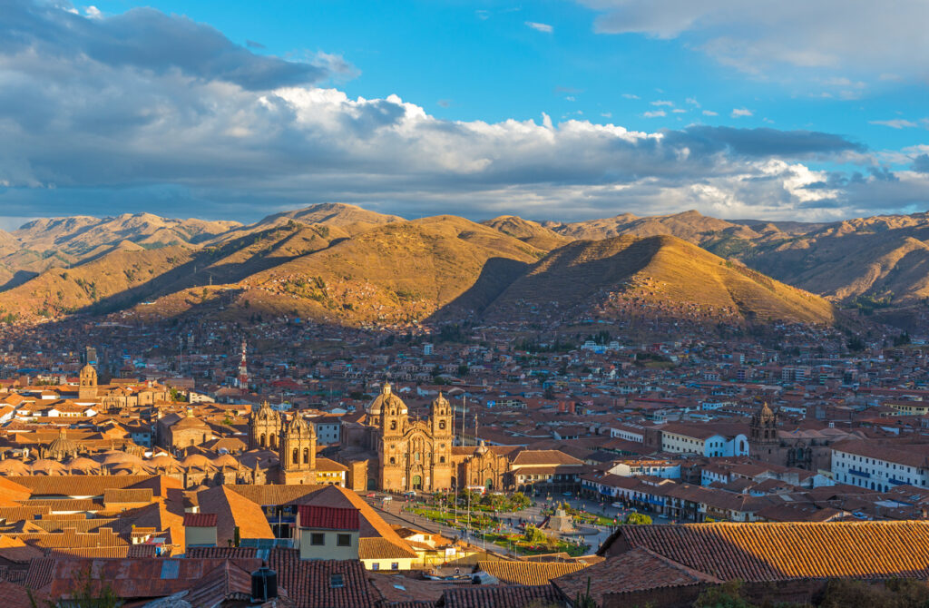 Panorama über die roten Ziegeldächer von Cusco mit der Kathedrale und sonnenbeschienenen Andenhügeln.