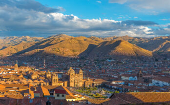 Panorama über die roten Ziegeldächer von Cusco mit der Kathedrale und sonnenbeschienenen Andenhügeln.
