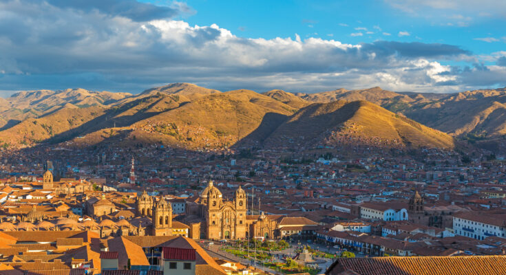 Panorama über die roten Ziegeldächer von Cusco mit der Kathedrale und sonnenbeschienenen Andenhügeln.