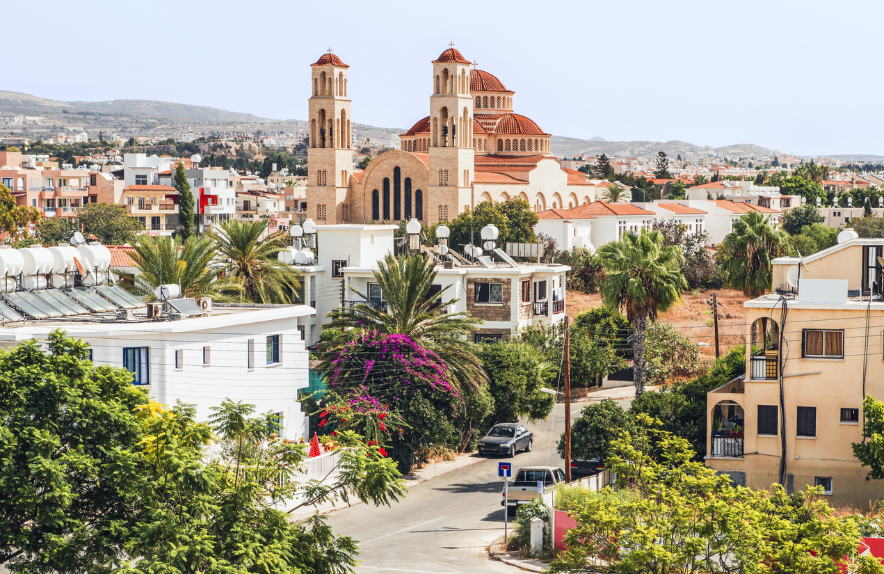 Blick über Paphos auf die orthodoxe Kathedrale Agioi Anargyroi mit roten Kuppeln zwischen Palmen.