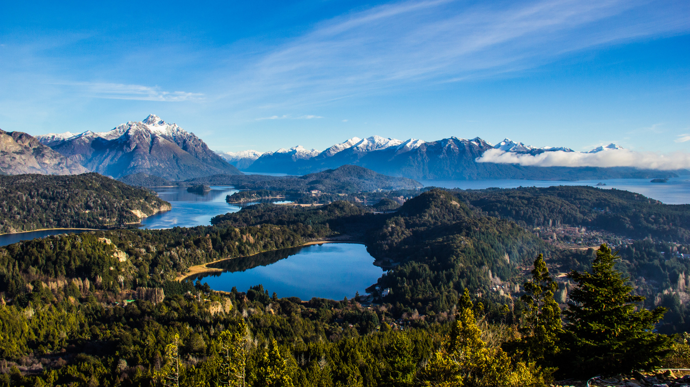 Panorama mit mehreren funkelnden Seen, bewaldeten Hügeln und schneebedeckten Andenketten.