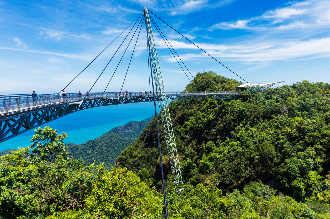 Fußgänger überqueren die schwebende Sky Bridge hoch über dem grünen Regenwald mit Blick auf das blaue Meer.