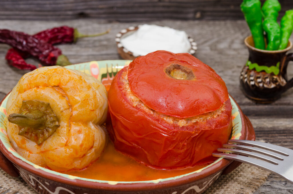 Ein Teller mit einer gefüllten Paprikaschote und einer gefüllten Tomate in Soße als ungarisches Gericht, gefüllte Paprikaschoten.