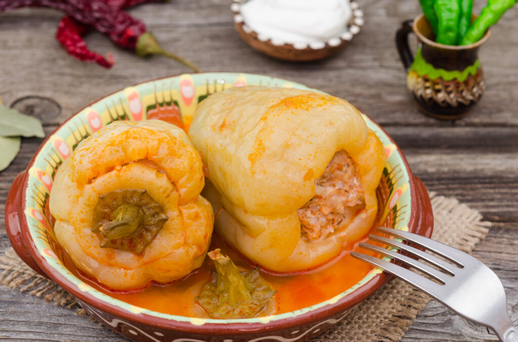 Zwei weich geschmorte gefüllte Paprikaschoten in tomatiger Soße als typisches ungarisches Gericht auf einem bunten Teller.