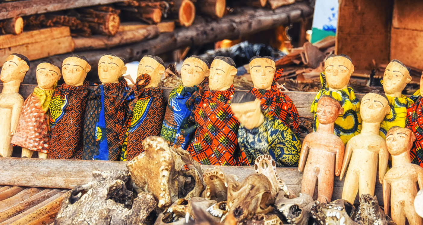 Reihe geschnitzter Holzpuppen in bunten Stoffen auf einem Marktstand in Kumasi, Ghana.