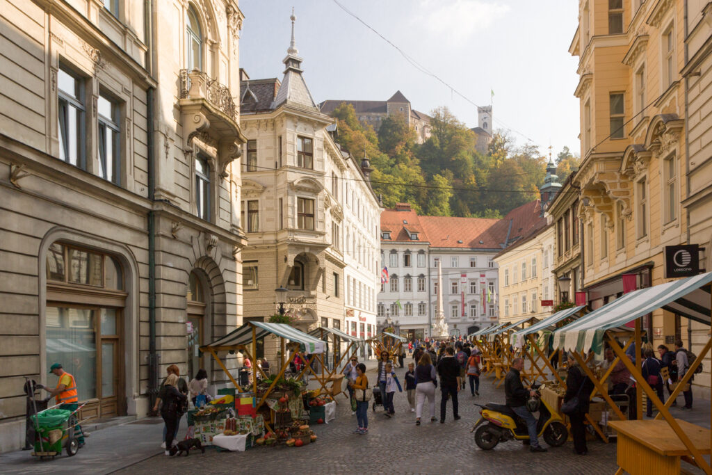 Straße in der Altstadt von Ljubljana mit Marktständen und Blick hinauf zur Burg.