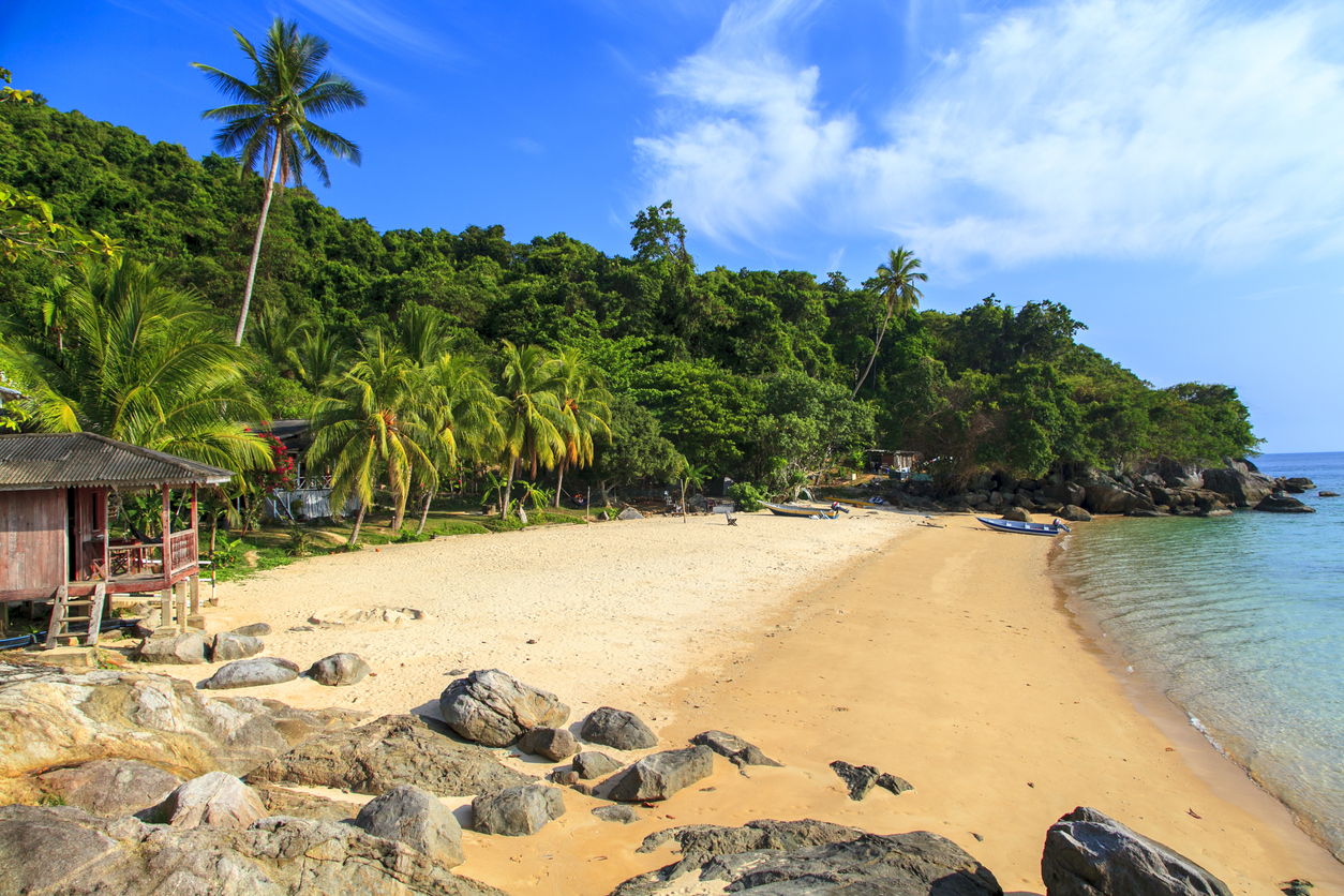 Ein heller Sandstrand auf den Perhentian Islands liegt zwischen Palmen, Dschungel und ruhigem Meer.