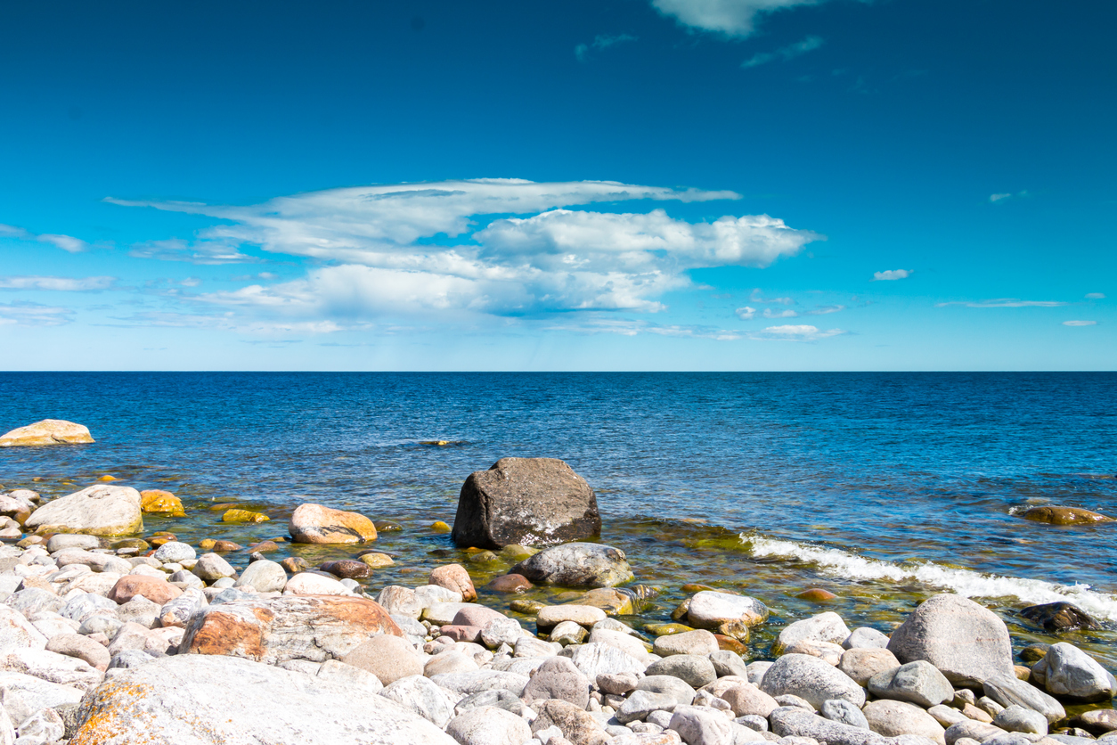 Ein steiniger Strand liegt am Ufer des Bottnischen Meerbusens vor ruhigem, blauem Wasser.