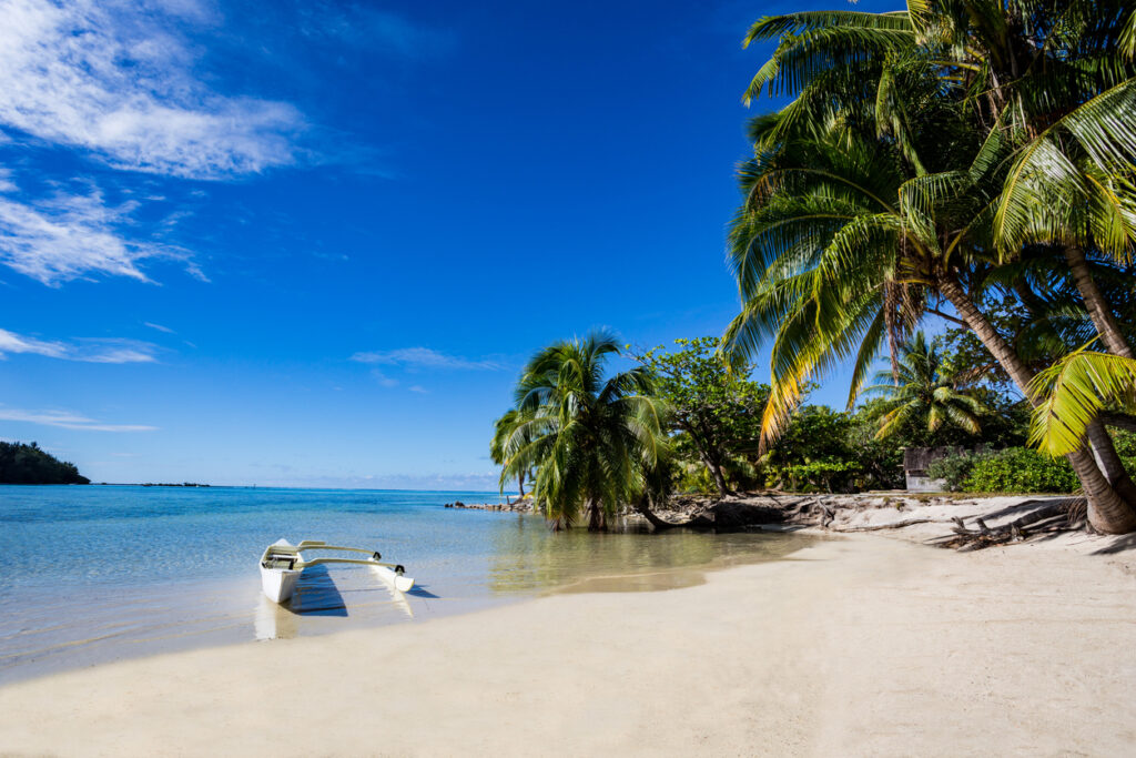 Kleines Auslegerboot liegt am flachen Strand in Französisch-Polynesien.
