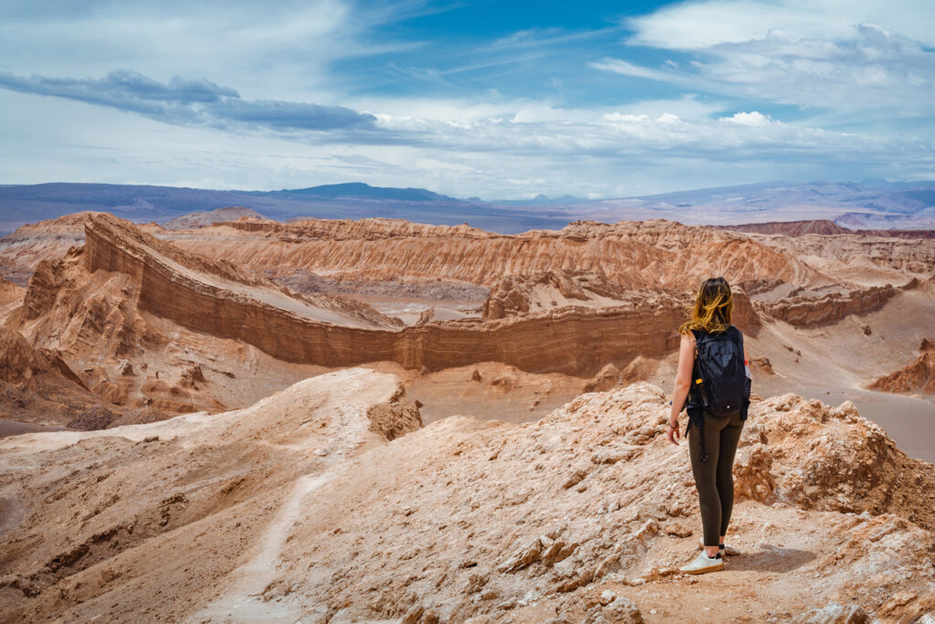 Eine Wanderin steht auf einem Felsplateau bei San Pedro de Atacama, Chile, und blickt über die Wüstenlandschaft.