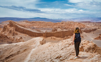 Eine Wanderin steht auf einem Felsplateau bei San Pedro de Atacama, Chile, und blickt über die Wüstenlandschaft.