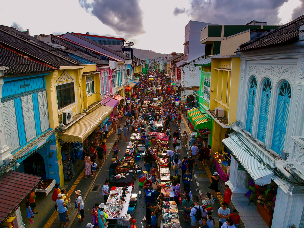 In der Altstadt von Phuket Town drängen sich Menschen zwischen Marktständen auf einer Fußgängerzone mit bunten Häusern.