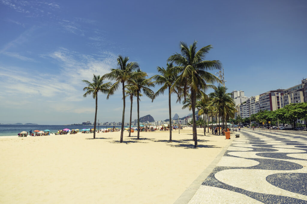 Sandstrand mit Palmen und der wellenförmigen Promenade von Copacabana in Rio de Janeiro.