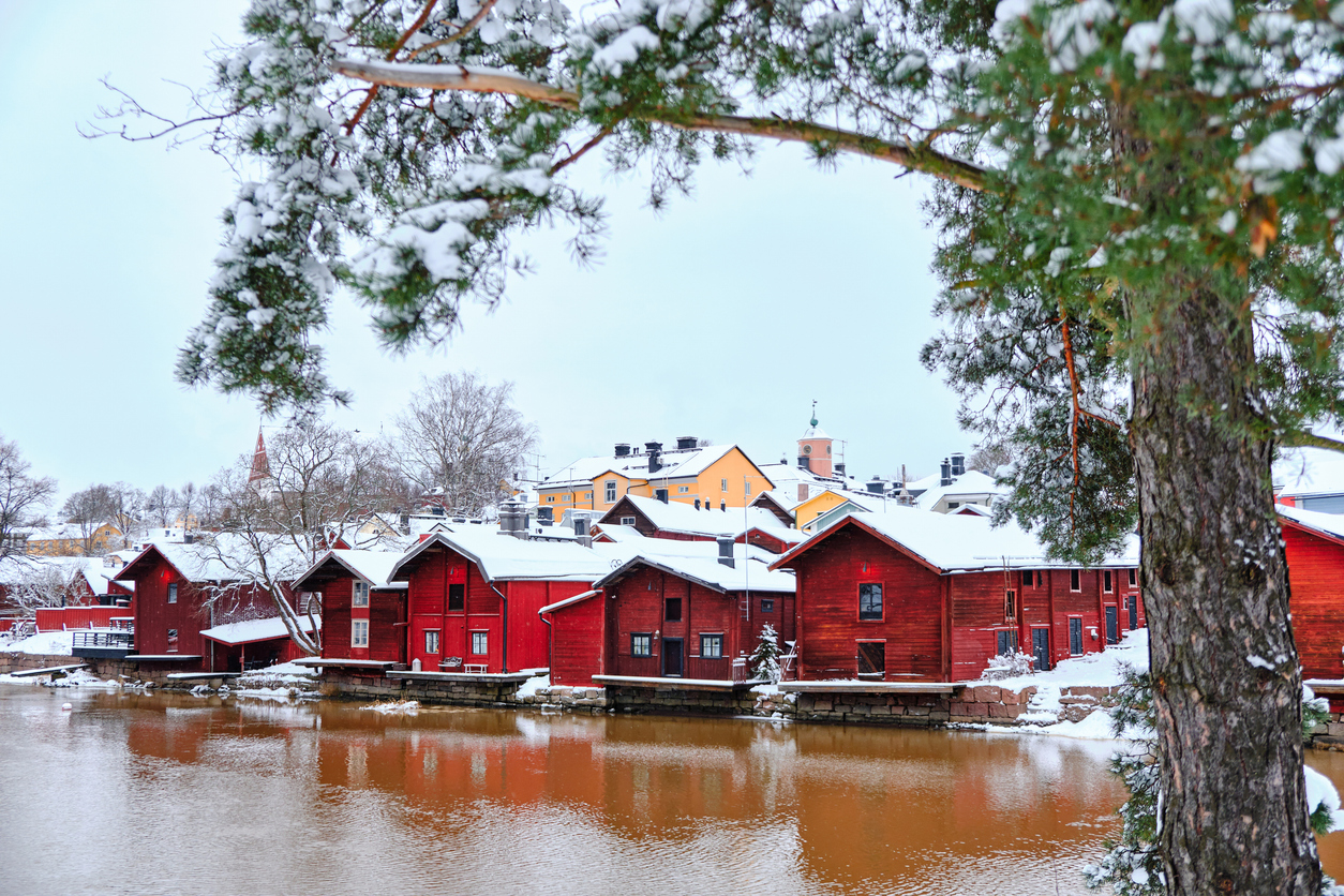 Verschneite rote Holzhäuser spiegeln sich im Fluss von Porvoo.
