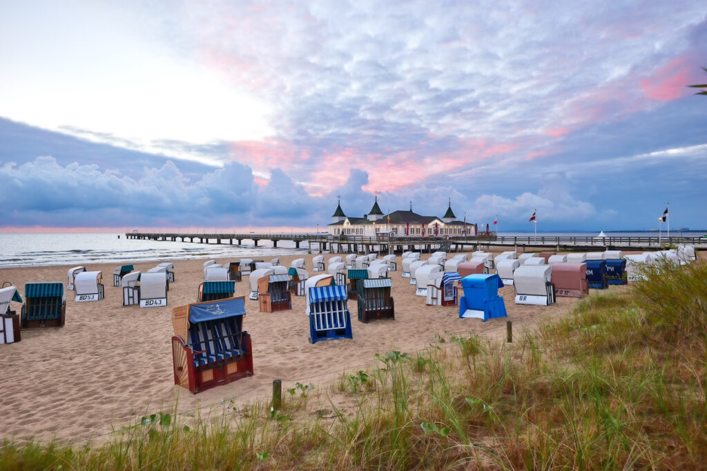 Viele Strandkörbe stehen am Strand von Ahlbeck vor der Seebrücke und einem rosa Himmel.
