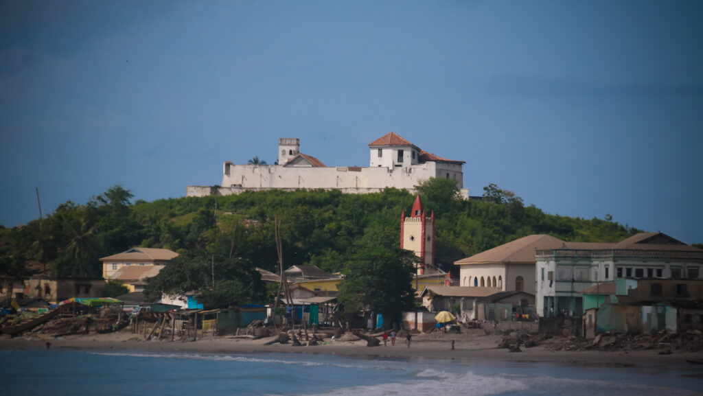 Weiße Küstenfestung auf einem grünen Hügel über dem Strand in Cape Coast & Elmina in Ghana.