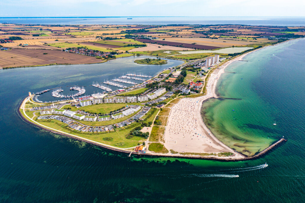 Luftaufnahme von Fehmarn mit Marina, Sandstrand, grüner Küstenlandschaft und türkisfarbenem Wasser.
