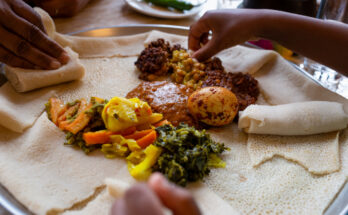 Hände greifen zu einem großen Teller mit Vegetarisches Injera-Menü mit Shiro, Linsen und Ei, dazu Gemüse und Soßen auf weichem Fladenbrot.