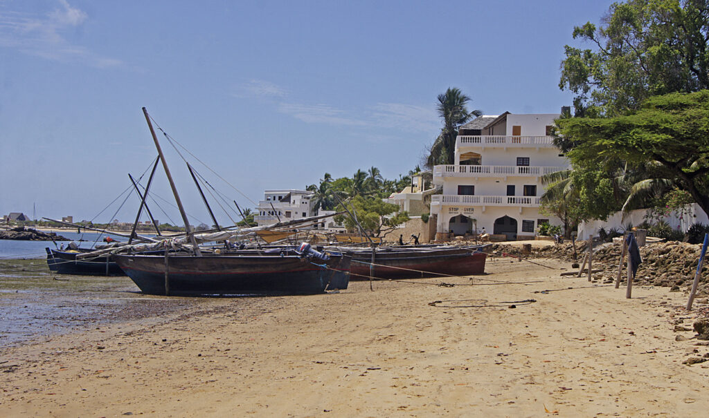 Traditionelle Holzboote liegen bei Ebbe vor weißen Häusern am Strand von Lamu, Kenia.