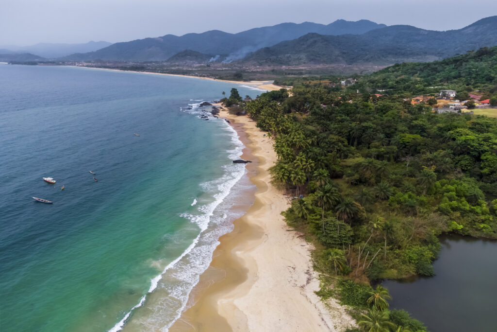 Langer tropischer Sandstrand mit Palmenwald und türkisfarbenem Meer in Sierra Leone.