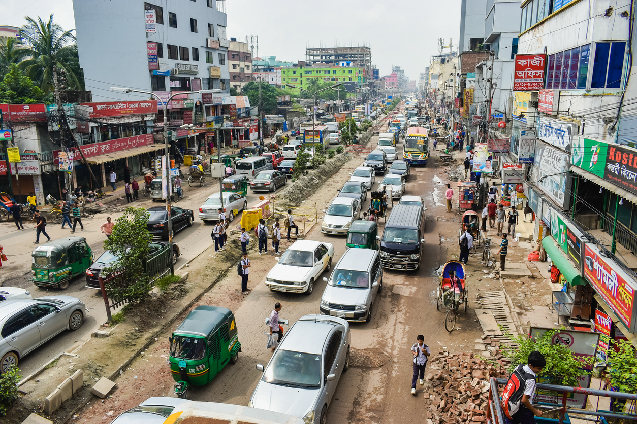 Belebte Hauptstraße in Dhaka mit vielen Autos, Rikschas und Fußgängern.