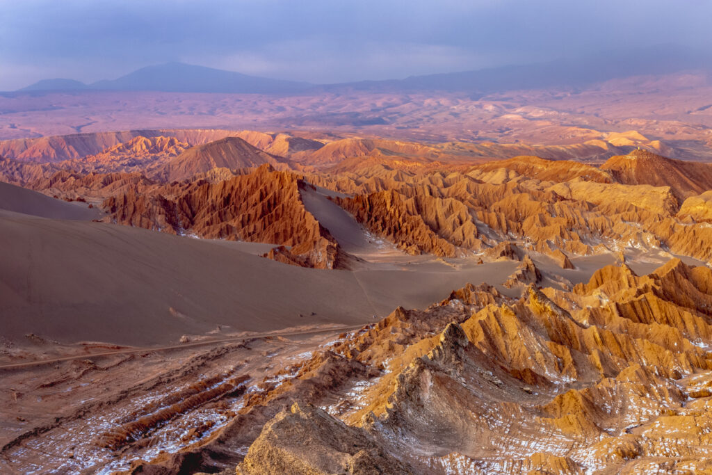 Ein Panorama aus Dünen und zerklüfteten Hügeln bei San Pedro de Atacama, Chile, leuchtet im Abendlicht.