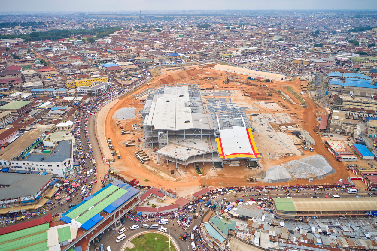 Luftaufnahme einer riesigen Marktbaustelle mit Hallen und umliegender Stadt in Kumasi, Ghana.