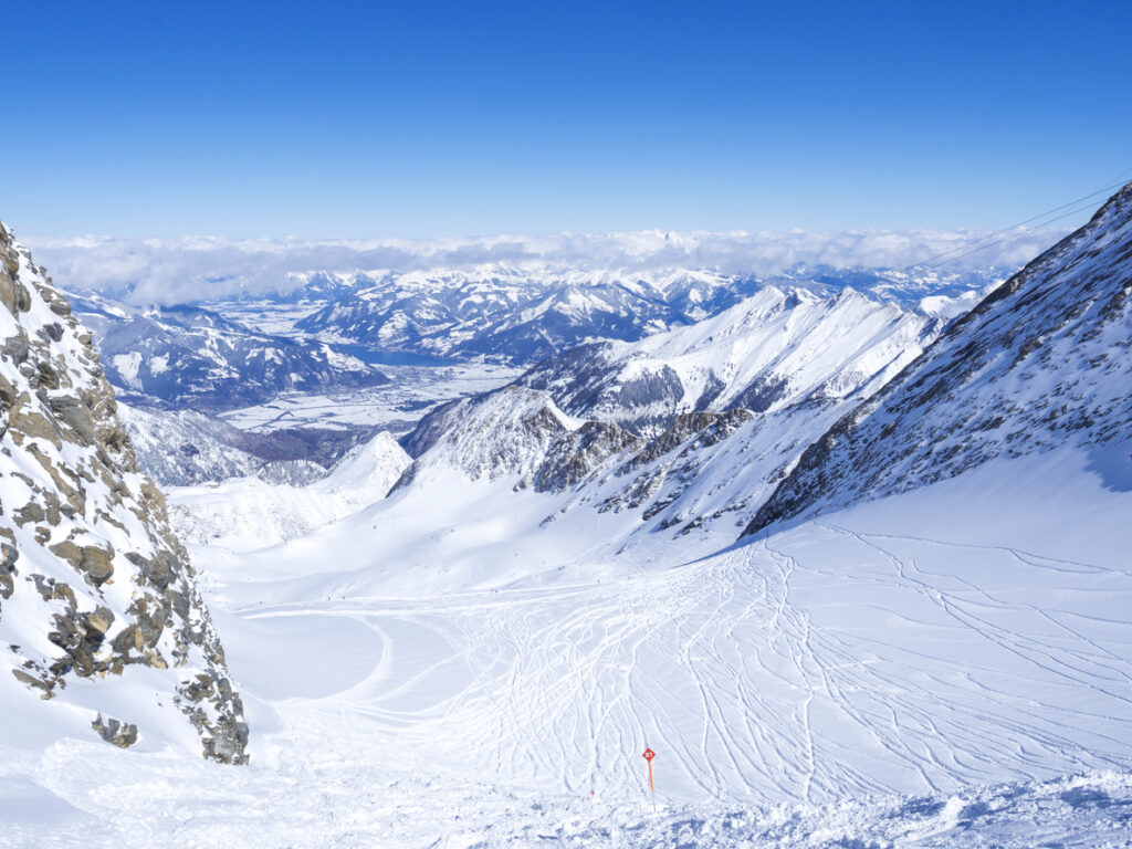 Blick von einer hohen Piste auf die verschneiten Berge und Täler rund um Zell am See.