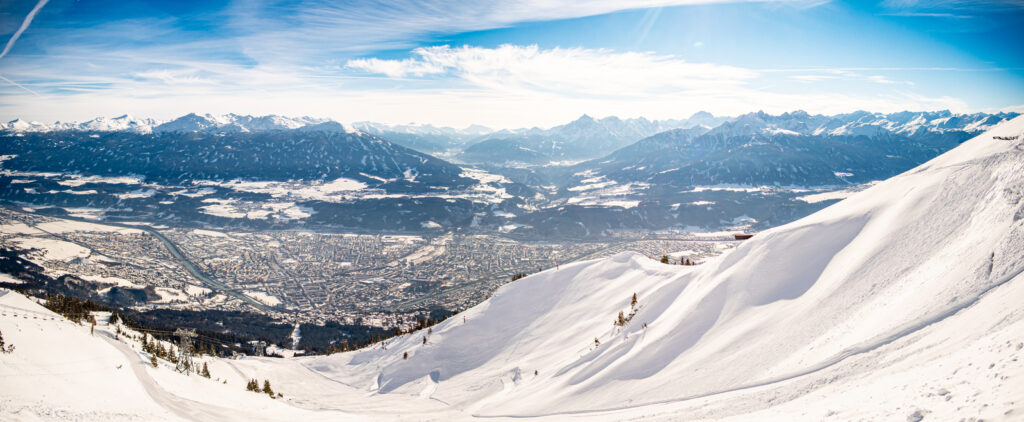 Blick von den verschneiten Bergen auf Innsbruck mit dem Inntal und den umliegenden Alpen.