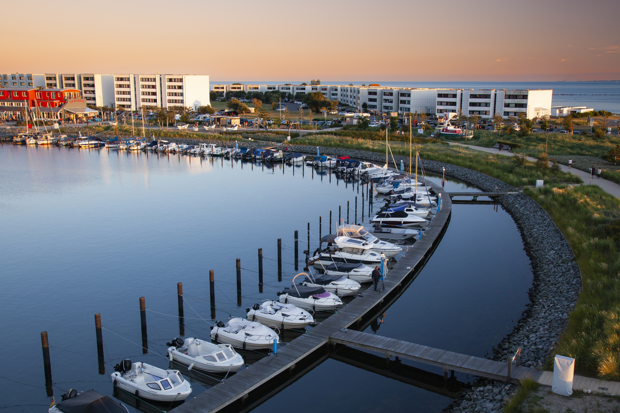 Boote liegen im Hafen auf Fehmarn, dahinter stehen Gebäude im warmen Licht der untergehenden Sonne.