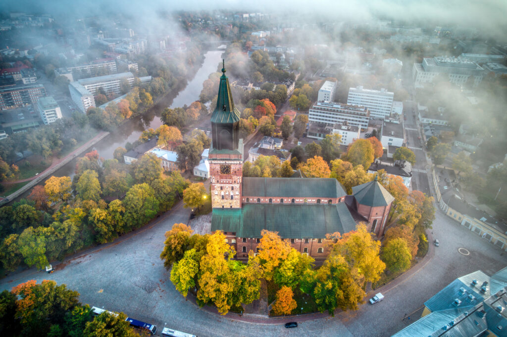 Luftaufnahme des Doms von Turku, umgeben von herbstlichen Bäumen und Nebel.
