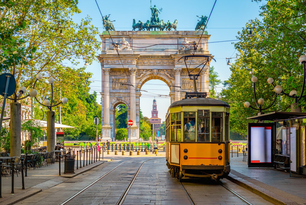 Eine gelbe Tram fährt in Mailand auf Schienen in Richtung Arco della Pace.