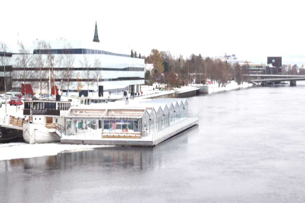 Verschneite Uferpromenade mit moderner Architektur und Steg am Fluss in Umeå.