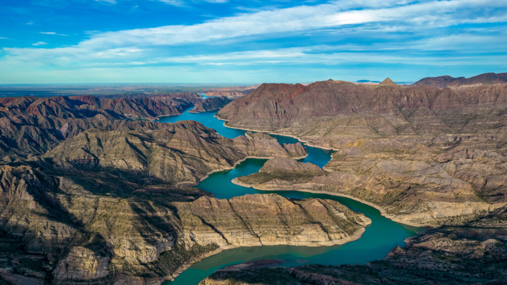 Luftaufnahme eines türkisfarbenen Stausees, der sich wie ein Fluss durch eine trockene Gebirgslandschaft nahe Mendoza windet.