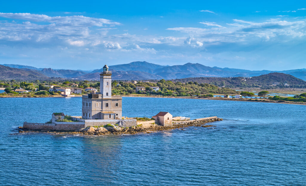 Alter Leuchtturm auf einer kleinen Insel vor Olbia auf Sardinien, umgeben von blauem Meer und Bergen im Hintergrund.