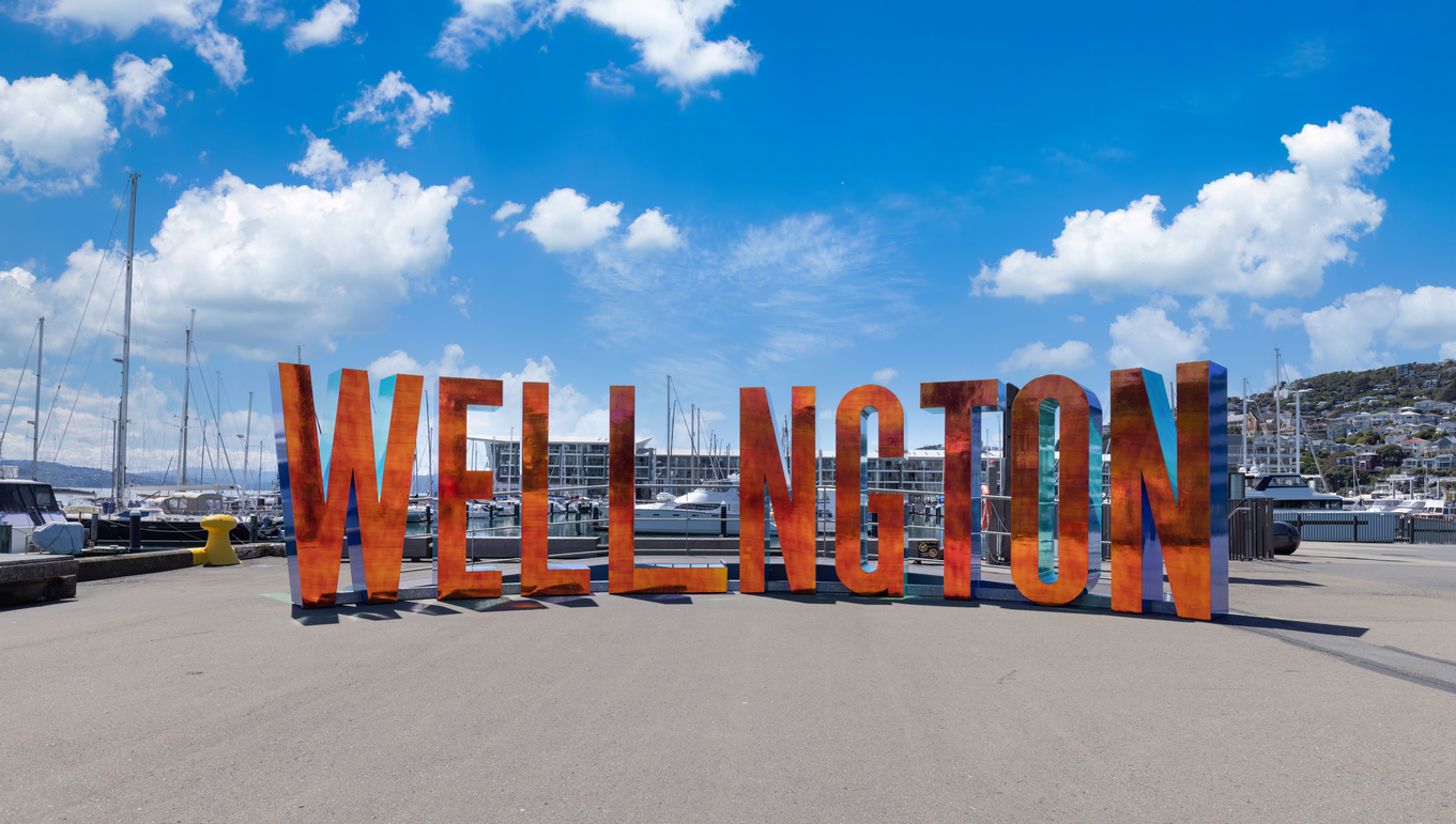 Großer bunter Wellington Schriftzug steht vor Yachthafen und blauem Himmel.