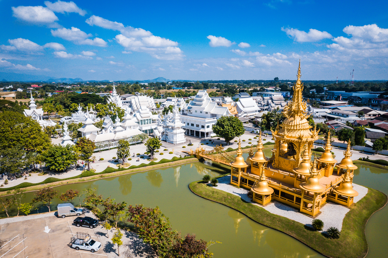 Luftaufnahme des goldenen Gebäudes und des weißen Wat Rong Khun bei Chiang Rai mit Wassergraben und Garten.
