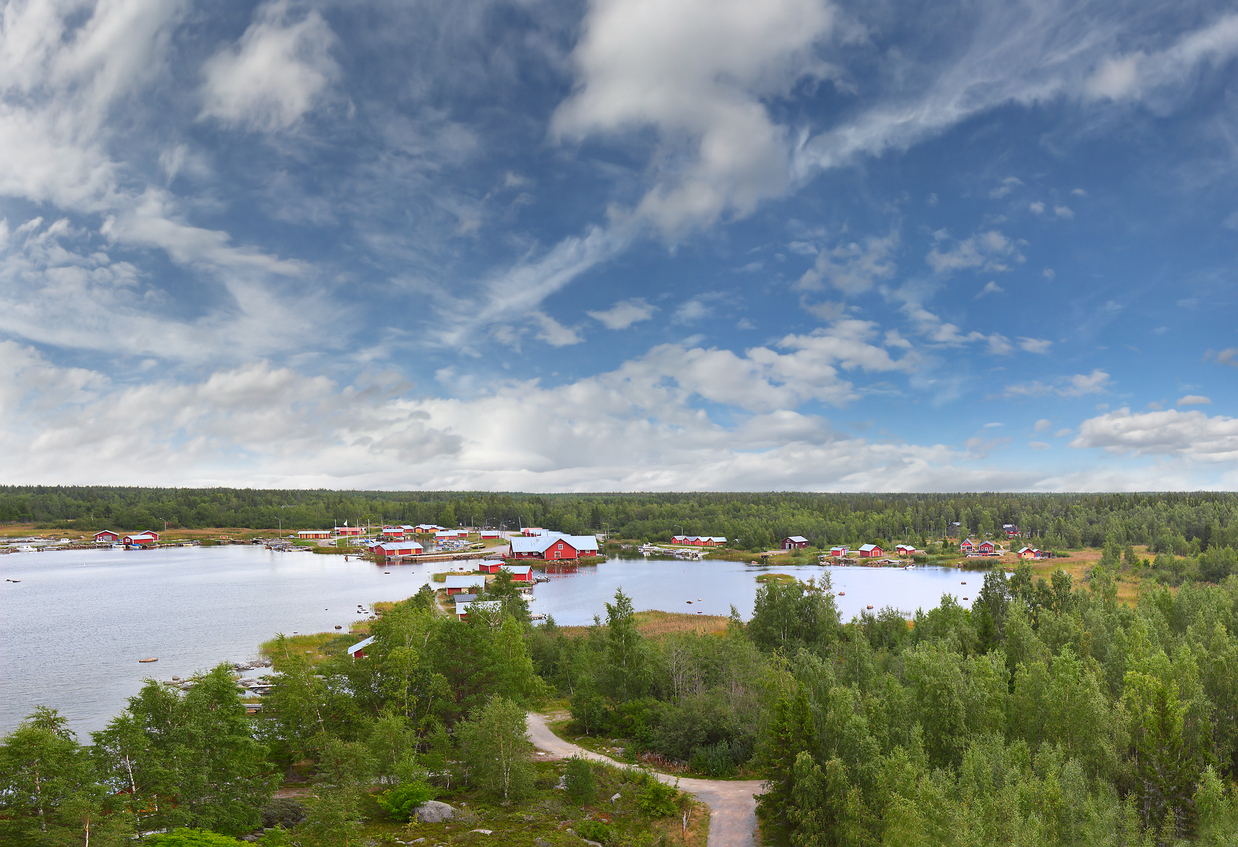 Weite Küstenlandschaft mit roten Häusern am Wasser im Kvarken-Archipel in Finnland.
