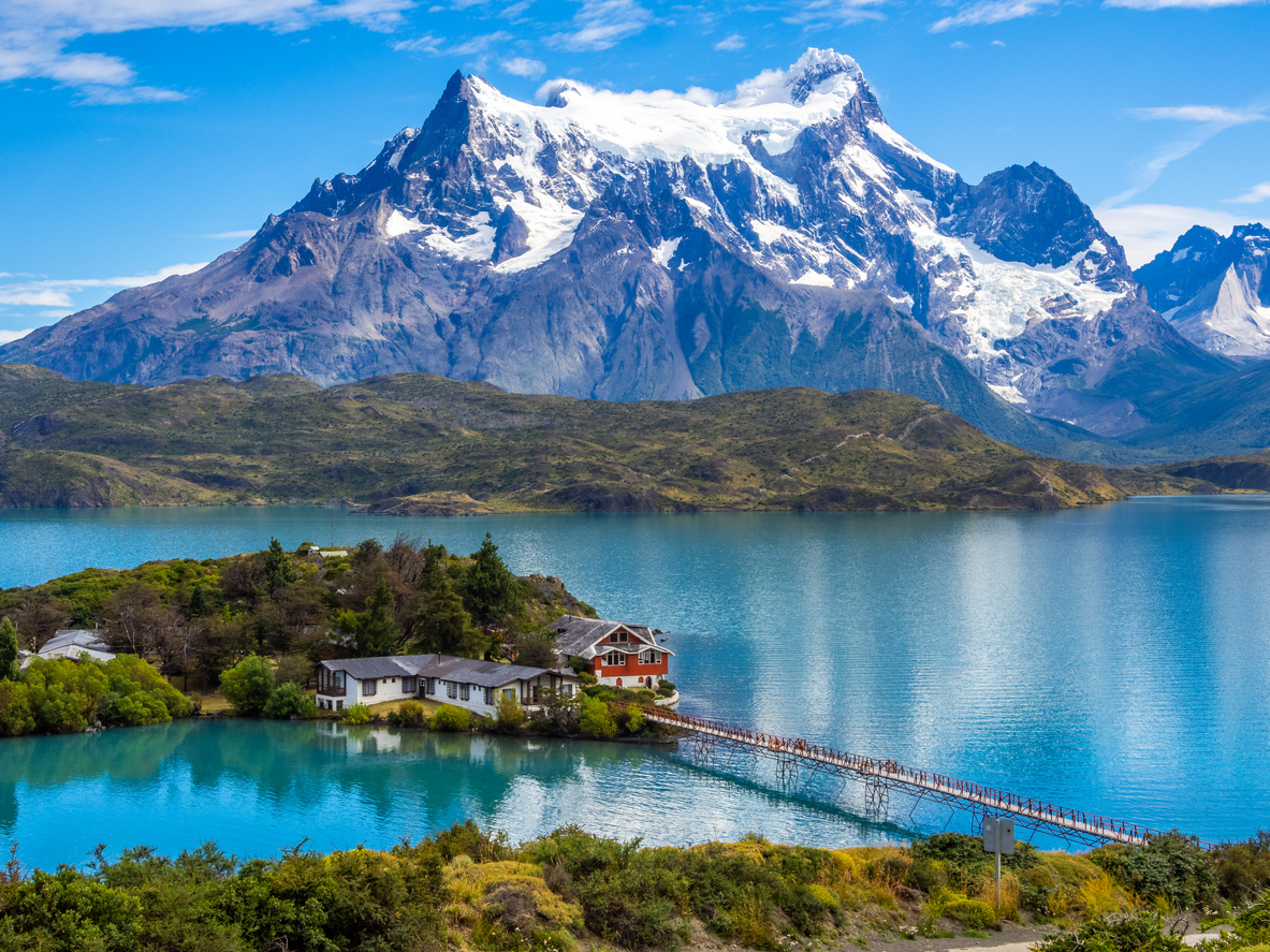 Ein türkisblauer See mit Lodge und Steg liegt im Torres del Paine Nationalpark, Chile, vor schneebedeckten Bergen.