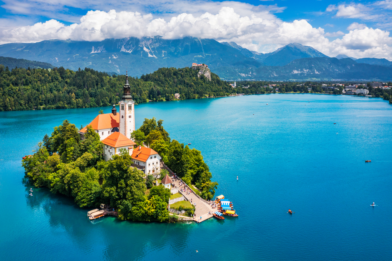 Panorama der Inselkirche im Bleder See in Bled mit Bergen und blauem Wasser im Hintergrund.