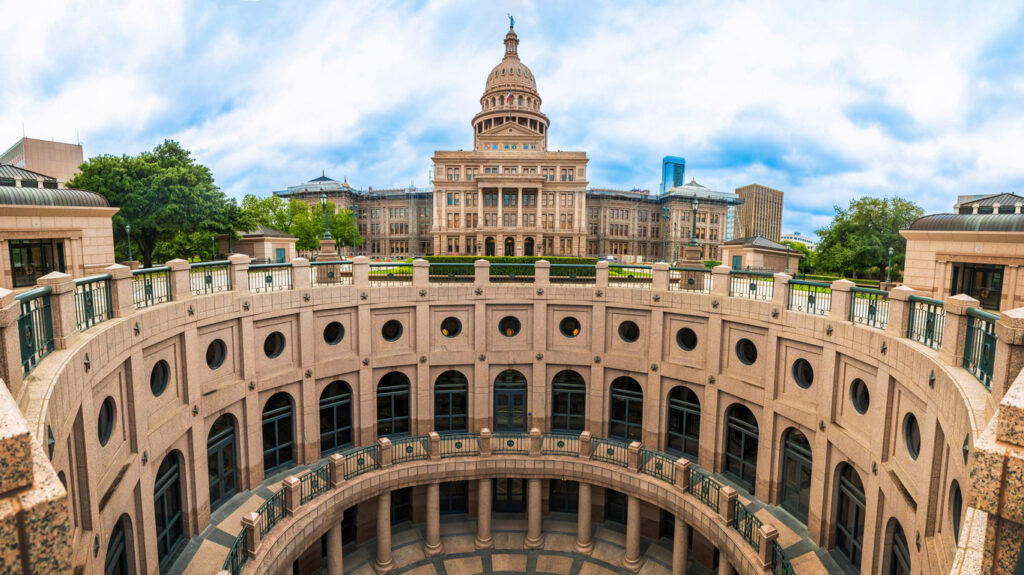 Weitwinkelaufnahme des Texas State Capitol mit dem runden Innenhof im Vordergrund an einem leicht bewölkten Tag in Austin, Texas.