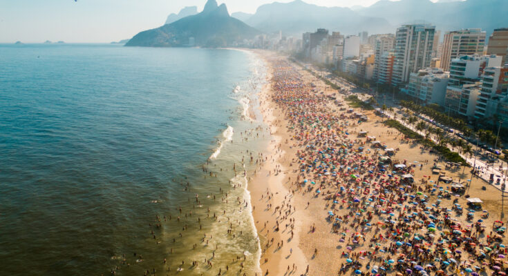 Menschenmassen tummeln sich am breiten Sandstrand und im Meer von Rio de Janeiro.