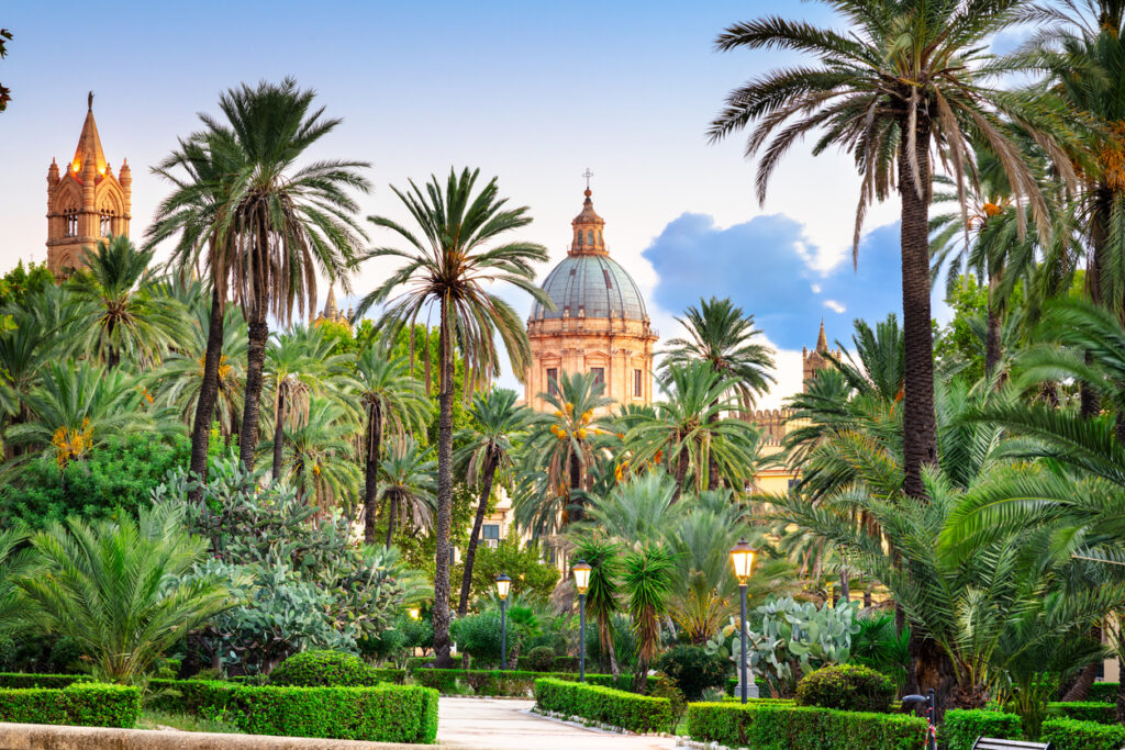 Grüner Park in Palermo mit hohen Palmen und einer Kuppel im Hintergrund.