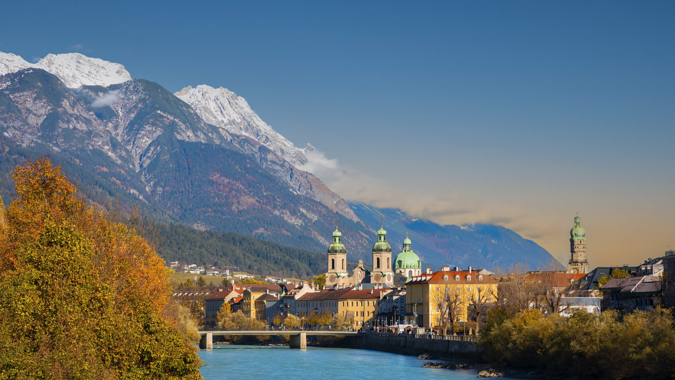 Die Stadt Innsbruck liegt am Inn, umrahmt von hohen Alpenbergen und herbstlich gefärbten Bäumen.