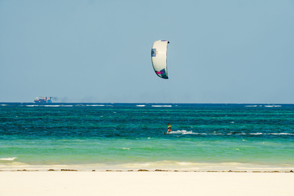 Ein Kitesurfer fährt auf dem türkisblauen Meer vor dem Diani Beach in Kenia.