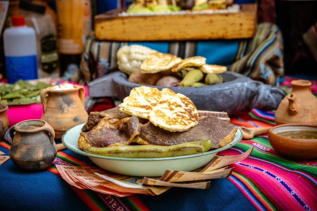 Ein Teller mit Fleisch, Beilagen und Käse liegt auf einem bunten Andentuch.