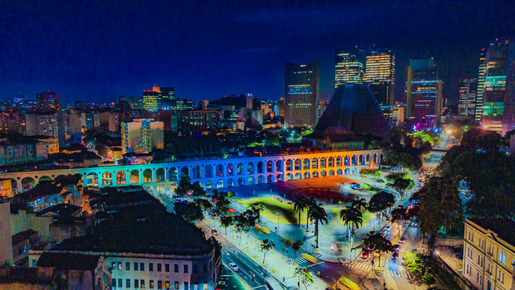 Blick auf die bunt beleuchtete Bogenbrücke Arcos da Lapa und die Innenstadt von Rio de Janeiro bei Nacht.