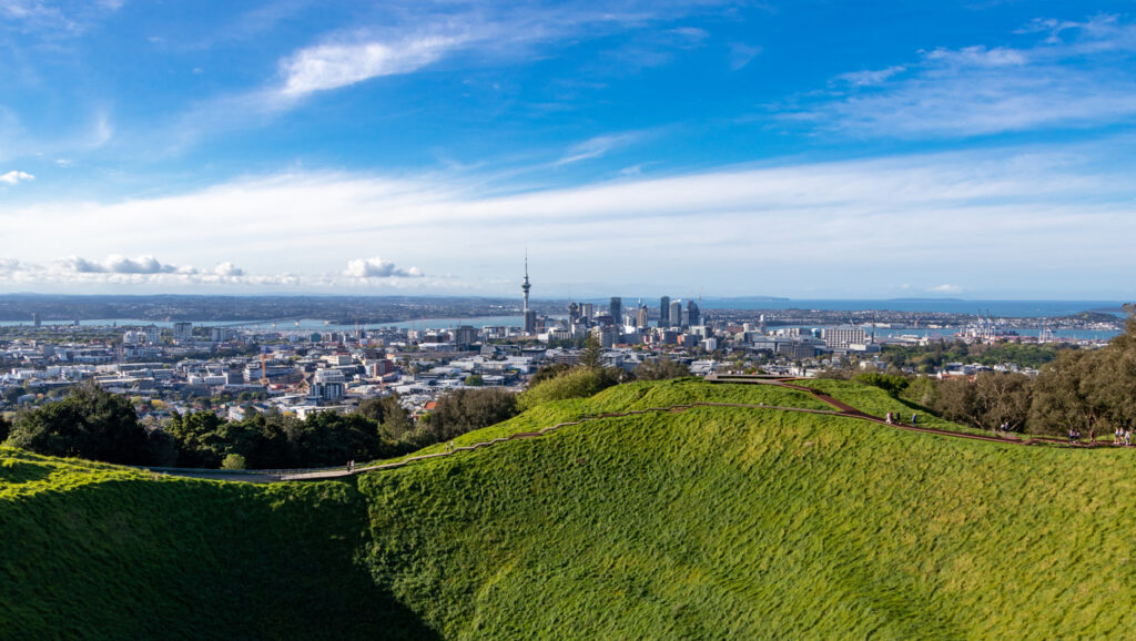 Panoramablick von einem grünen Vulkankrater auf die Skyline von Auckland und den Hafen.